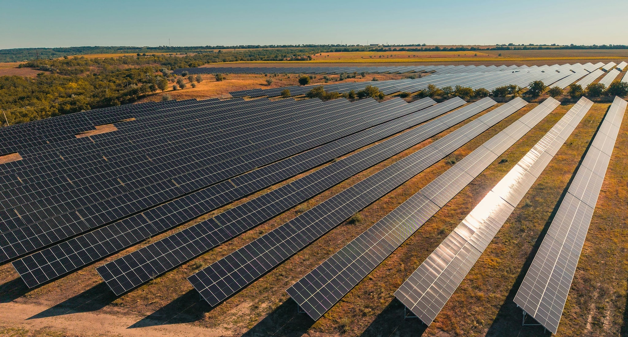 Aerial view of long rows of ground-mounted solar panels across dry open land